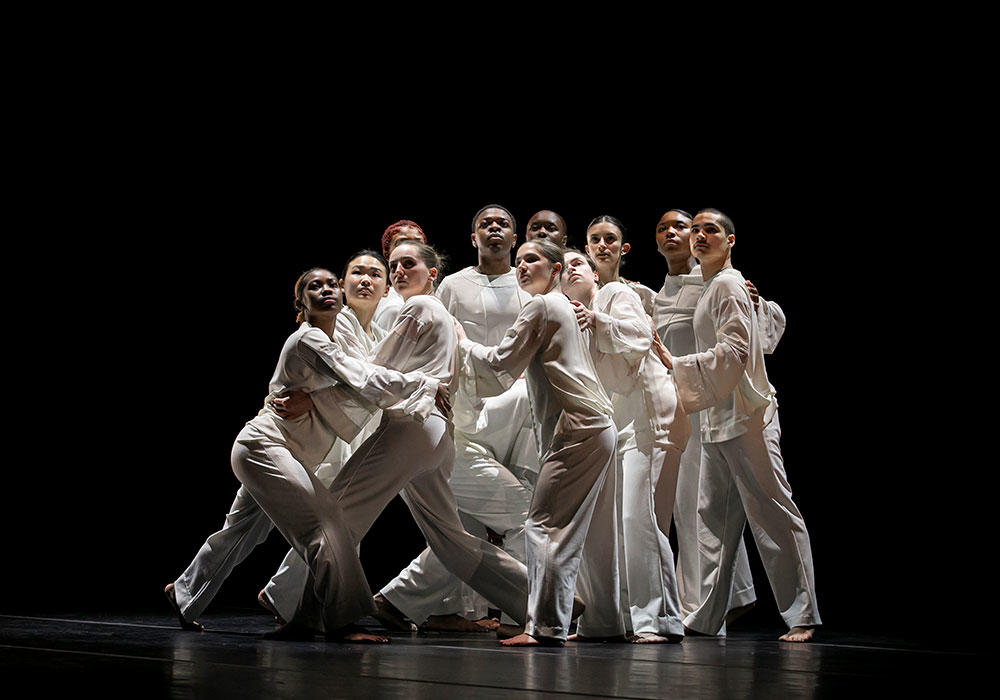 Mason dance students on stage dressed in white against black background
