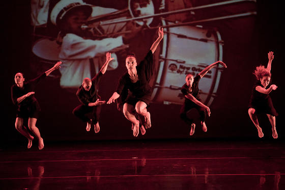 Dancers from the Camille A. Brown & Dancers company performing and leaping with large projected image behind them.
