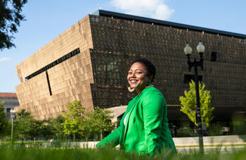 Mason alumna, Carla McGinnis, MA Arts Management ’13 standing outside her workplace, the National Museum of African American History and Culture. Read her story.